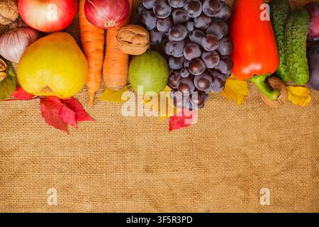 Flachlegung von verschiedenen frischen Herbstgemüsen, Früchten, Nüssen und Blättern, die oben auf einem rustikalen Sackleinenhintergrund arrangiert sind, mit großzügigem Kopierraum für Stockfoto