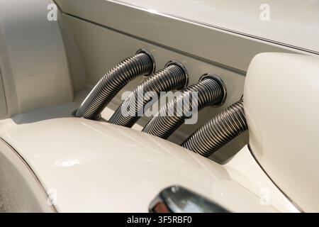 Berlin, Deutschland - 3. Mai 2026. Nahaufnahme von vier gerippten Chromauspuffrohren, die in die Seite eines weißen neoklassizistischen Luxusautos bei Oldtim integriert sind Stockfoto