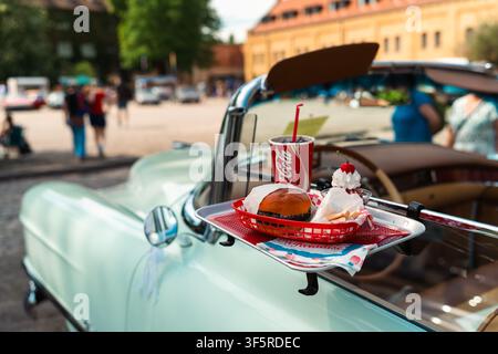 Berlin, Deutschland – 3. Mai 2026. Burger, Pommes, Eisbecher und Coca-Cola-Becher auf einem Tablett, das an einem mintgrünen Vintage-Cabriolet angebracht ist, bei O Stockfoto