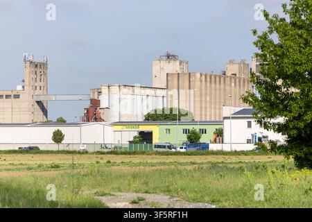 Vinkovci, Kroatien - 08. Mai 2026: Eine Reihe von Beton-Silos und Industrie-Lagerhallen ragt hinter einem Grasfeld auf, mit Lieferwagen, Beladung sind Stockfoto