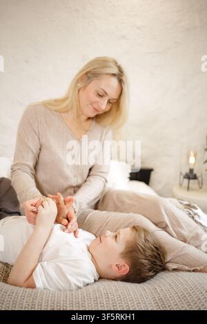 Eine fürsorgliche Mutter hält sanft die Hände ihres Sohnes und zeigt Liebe und Zuneigung in einer gemütlichen Indoor-Umgebung, perfekt für Muttertagsthemen und familienorientierte Stockfoto