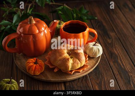 Ein charmantes Stillleben mit einer kürbisgeformten Teekanne und einer passenden Kaffeetasse, gefüllt mit dunkler Flüssigkeit, begleitet von einem dekorativen Gebäck und Mini p Stockfoto