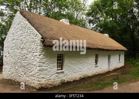 Traditionelles strohgedecktes weiß getünchtes Cottage, eingebettet in Waldlandschaft im Ulster American Folk Park nahe Omagh, County Tyrone, Nordirland. Stockfoto