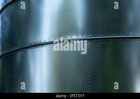 Nahaufnahme einer genieteten Metall-Tankkonstruktion mit gebogenen Verbindungen und reflektierender Oberfläche. Stockfoto