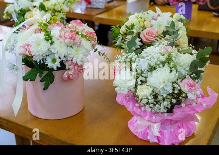 Menschen erstellen Blumenarrangements in Vasen auf Holztischen während eines Kurses. Die Umgebung ist fröhlich und voller Farbe. Stockfoto