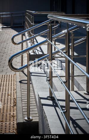 Ein outdoor Edelstahl-Geländer steht auf Betonstufen in der Nähe eines modernen Gebäudeeingangs installiert. Die glänzende Metallstruktur bietet Sicherheit Stockfoto
