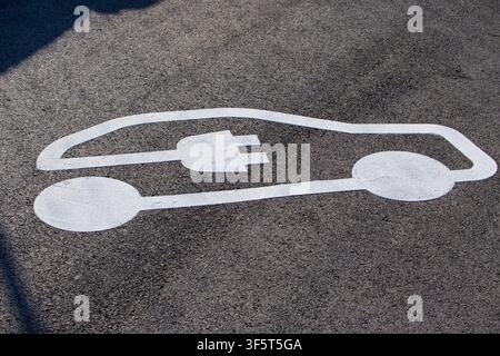 Elektrofahrzeug-Ladestation-Symbol, Nahaufnahme, in Weiß auf dunkler Asphaltstraßenoberfläche gemalt, markiert einen reservierten EV-Parkplatz für grüne Mobilität Stockfoto