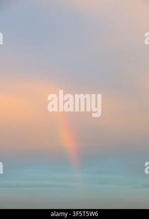 Weicher pastellfarbener Himmel mit zartem Regenbogen über ruhigem Horizont Stockfoto