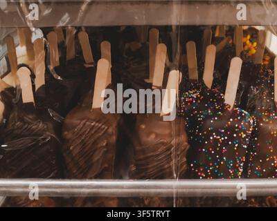 Verschiedene schokoladenüberzogene Eisriegel auf Stäbchen mit Streuseln in einer Vitrine Stockfoto