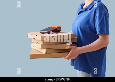 Lieferperson in blauer Uniform hält einen Stapel Pizzakartons mit einem Zahlungsterminal oben drauf, isoliert auf einem hellblauen Hintergrund Stockfoto