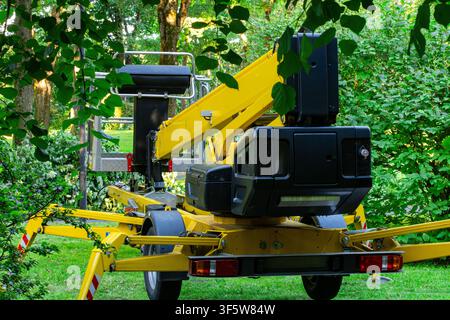 Gelbe Hebebühne mit erhöhtem Auslegerarm, schwarzer Steuerbox und Metallkorb, steht auf grüner Wiese mit ausgefahrenen Auslegern, rot weiß Stockfoto