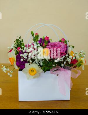 Farbenfrohes Blumenarrangement in einem weißen Korb auf einem Holztisch Stockfoto