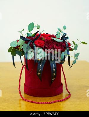 Strauß roter Rosen mit Bändern und Grünzeug in einer runden Schachtel auf einem Tisch Stockfoto