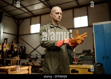 Männlicher Schweißer, der in einer Industriewerkstatt Schutz Handschuhe anzieht Stockfoto