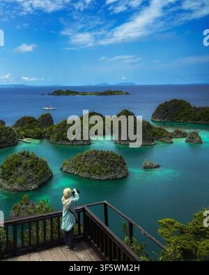 Eine Reisende macht Fotos der ikonischen Karstinseln und des türkisfarbenen Meeres vom hölzernen Aussichtspunkt in Piaynemo in Raja Ampat, Indonesien Stockfoto