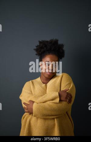 Porträt einer jungen afroamerikanischen Frau, die mit verschränkten Armen lächelt und Selbstliebe und psychisches Wohlbefinden repräsentiert, ideal für Gesundheits- und Lebensstil-Kampagnen, vertikal Stockfoto