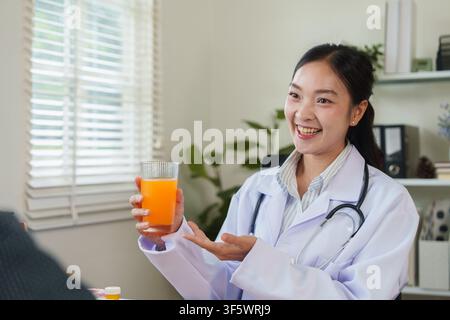 Lächelnde asiatische Ärztin hält ein Glas Orangensaft während einer Ernährungsberatung Stockfoto