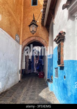Schmale Kopfsteinpflastergasse mit blauen und ockergelben Wänden und einem gewölbten Tor in Chefchaouen, Marokko. 4. August 2025. Stockfoto