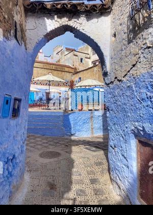Schmale Kopfsteinpflastergasse mit blauen und ockergelben Wänden und einem gewölbten Tor in Chefchaouen, Marokko. 4. August 2025. Stockfoto