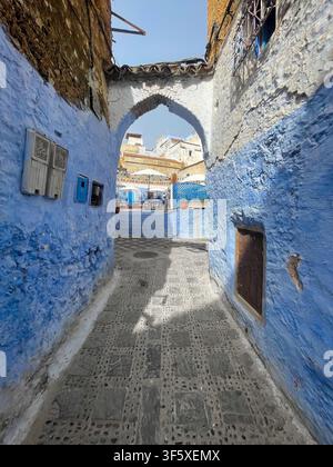 Schmale Kopfsteinpflastergasse mit blauen und ockergelben Wänden und einem gewölbten Tor in Chefchaouen, Marokko. 4. August 2025. Stockfoto