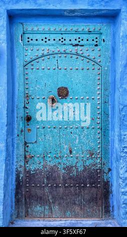 Verwitterte blaue Holztür mit Metallnieten und gewölbtem Design in der Medina von Chefchaouen, Marokko. 4. August 2025. Stockfoto