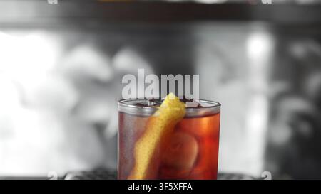 Erfrischender roter Cocktail mit einer Zitronenspirale und Eis, bereit zum Trinken in einer schwach beleuchteten Barszene Stockfoto