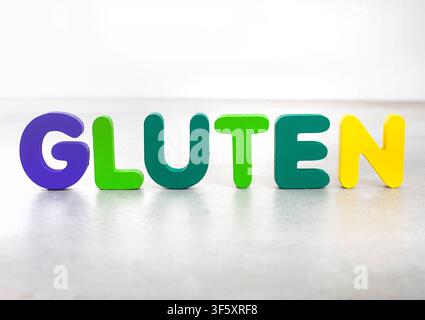 Das Wort Gluten, geschrieben mit bunten Holzalphabetbuchstaben auf einem neutralen Hintergrund. Geeignet für glutenfreie Ernährung, Ernährung, Nahrungsmittelallergien, Zeli Stockfoto