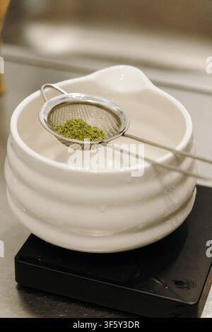Frisch gesiebtes Matcha-Pulver ruht in einem feinen Mesh-Sieb über einer Keramikschale. Traditionelle Teezubereitung, die Premium-Grünthee hervorhebt und Stockfoto