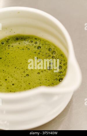 Nahaufnahme von frisch zubereitetem Matcha-Tee mit glattem Schaum in einer Keramikschale. Traditioneller japanischer grüner Tee servierfertig. Stockfoto