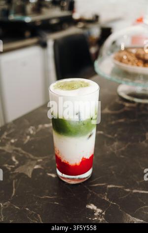 Fertiger Eistee mit Erdbeere und Matcha in lebendigen roten, weißen und grünen Schichten in einem klaren Glas. Erfrischendes Spezialkaffeedrink auf Marmor Stockfoto