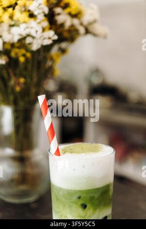 Schichtweiser Erdbeer-Matcha-Latte mit cremiger Sahnehaube, serviert mit einem gestreiften Papierstrohhalm. Erfrischendes Spezialkaffegetränk im Nahaufnahme. Stockfoto