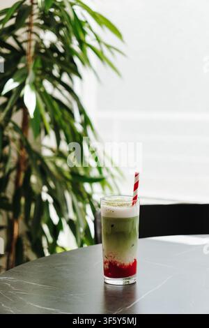 Frisch zubereiteter Eistee mit Erdbeere und Matcha, serviert auf einem Tisch in der Nähe eines hellen Fensters in einem modernen Café. Erfrischendes Spezialgetränk mit natürlichem Stockfoto