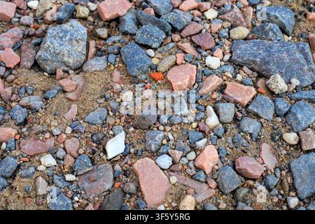 Nahaufnahme der Textur aus gemischtem Granitkies, roten Steinfragmenten und Sand auf dem Boden. Konzept der Geologie, Landhintergrund und Baumaterial. Stockfoto