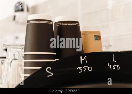Gestapelte To-go-Kaffeebecher, die hinter der Theke des Cafés angeordnet sind, bereit zum Servieren von heißen Getränken. Kaffeehaus-Essentials in einem modernen Interieur. Stockfoto