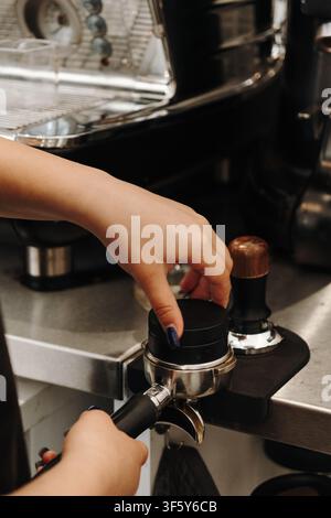 Barista komprimiert frisch gemahlenen Kaffee mit einem Tamper vor dem Brühvorgang von Espresso. Wesentlicher Schritt in der Zubereitung von Spezialkaffee. Stockfoto