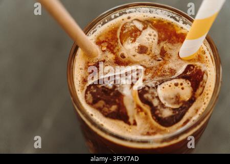 Nahaufnahme eines erfrischenden Eiskaffees mit Orangensaft, Eiswürfeln und Papierstrohhalmen. Strukturierte Oberfläche eines geschichteten Spezialkaffees. Stockfoto