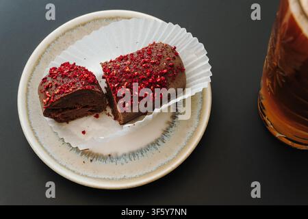 Nahaufnahme eines schokoladenüberzogenen Desserts, bedeckt mit gefriergetrockneten Himbeerstücken auf weißem Backpapier. Reichhaltiges handgefertigtes Gebäck mit Platz für Text. Stockfoto