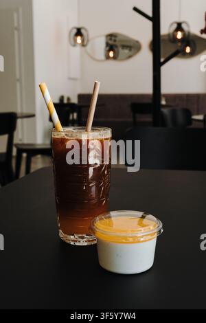 Eiskaffee serviert mit Vanille-Panna-Cotta, gekrönt mit Mangosauce in einem modernen Café. Zeitgenössisches Interieur schafft eine gemütliche Atmosphäre mit Kopierraum. Stockfoto