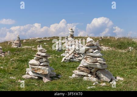 In Italien umgeben verstreute Felsen und grünes Gras eine Gruppe von Steinanhäufungen auf dem Monte Baldo. Die ausgeglichenen Formationen stehen unter einem hellen Sommerhimmel i Stockfoto