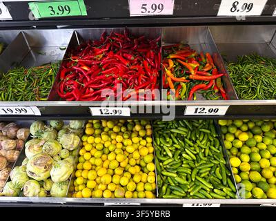 Helle Auslage mit frischem Gemüse, darunter Paprika, Limetten und Zwiebeln, die in den Regalen eines Supermarkts arrangiert sind. Stockfoto