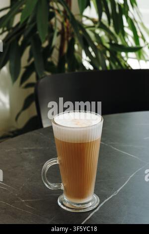 Frisch zubereiteter Latte mit seidigem Milchschaum, serviert in einer klaren Glastasse auf einem modernen Cafétisch. Minimale Kaffeekomposition mit großzügigem Kopierraum. Stockfoto