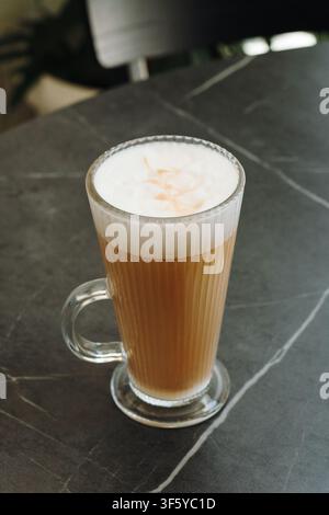 Frisch zubereiteter Latte mit seidigem Milchschaum, serviert in einer klaren Glastasse auf einem modernen Cafétisch. Minimale Kaffeekomposition mit großzügigem Kopierraum. Stockfoto