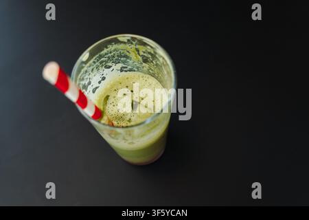 Halb fertiger Eismatcha-Latte mit Eiswürfeln und einem gestreiften Papirostrohhalm in einem klaren Glas. Erfrischendes grünes Teegetränk, serviert in einem modernen Café. Stockfoto