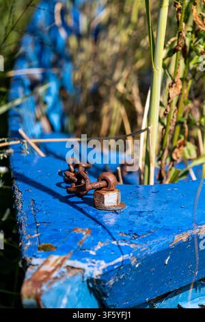 Nahaufnahme eines alten, lebendigen blauen Bootes, das am Wasserrand ruht. Ein rostiger Metallbügel sitzt auffällig auf der abgeblätterten Farbe und deutet auf seine Ma Stockfoto