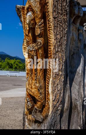 Nahaufnahme einer kunstvollen Holzskulptur, die direkt in einen großen Baumstamm geschnitzt wurde. Die Skulptur stellt ein stilisiertes Gesicht mit detaillierten Fe Stockfoto