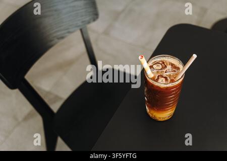 Erfrischender Eiskaffee mit Orangensaft in einem dekorativen Glas auf einem Cafétisch serviert. Minimale Komposition mit moderner Präsentation. Stockfoto
