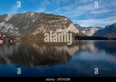 Ruiges alpines See Hallstatt, Österreich, mit Spiegelungen von Bergen und traditionellen Bootshäusern unter einem blauen Himmel. Stockfoto