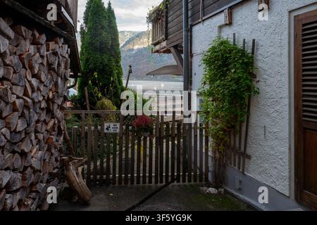Eine gemütliche Küstenstraße mit einem Holztor, gestapeltem Feuerholz, einem Balkon und Blick auf die Berge am Hallstättersee in Österreich. Stockfoto