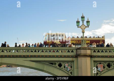 Touristen auf der Westminster Bridge in London mit einem offenen Big Bus Sightseeing-Tour, der unter einem klaren blauen Himmel vorbeifährt. Stockfoto