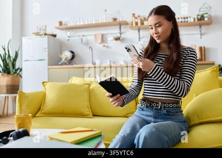 Eine junge Frau konzentriert sich auf ihr Smartphone, während sie auf einem lebhaften gelben Sofa sitzt Stockfoto